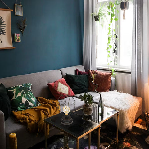 Lampada da tavolo con volto astratto in metallo nero su tavolino vetro in soggiorno colorato con parete blu e cuscini decorativi